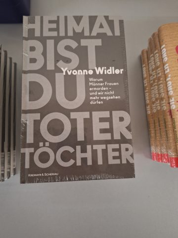 Ein Buchstapel auf einem Tisch. Das Buch heißt "Heimat bist du toter Töchter" von Yvonne Widler. Der Einband ist schwarz mit grauem Text