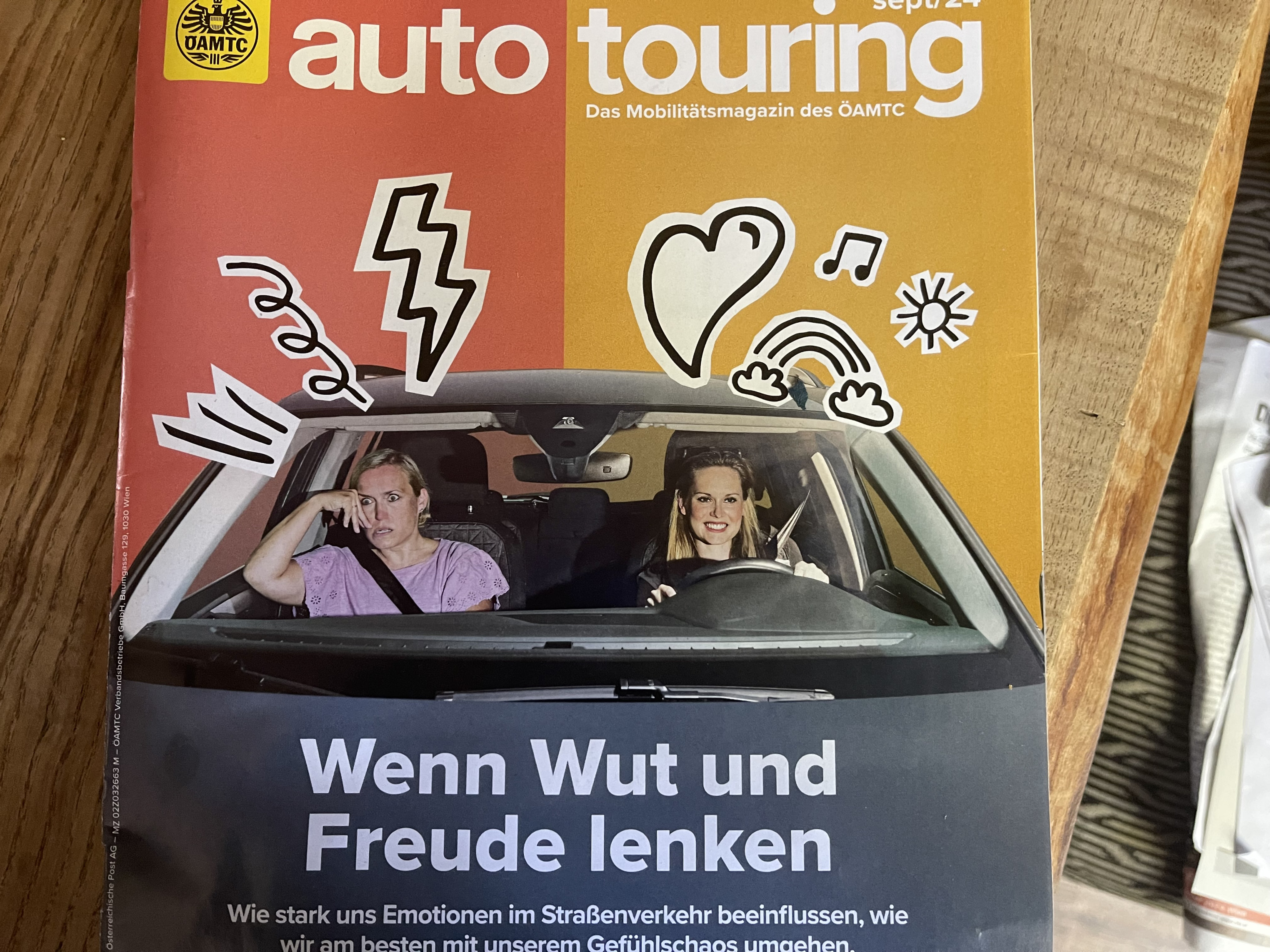 2 Frauen sitzen in einem Auto. Die Beifahrerin schaut genervt, die Fahrerin glücklich. Es handelt sich um das Cover der Zeitschrift auto touring. Unter den Frauen steht der Titel der Coverstory: Wenn Wut und Freude lenken.